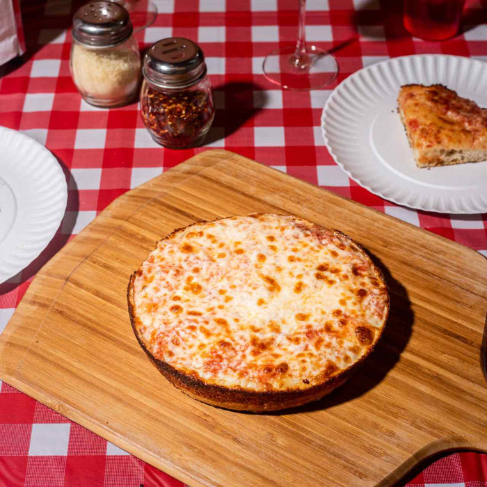 Pizza in teglia con salsa di pomodoro e mozzarella su un tagliere di bambù Ooni su un tavolo con piatti e fette di pizza.