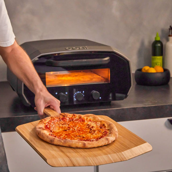 Una pizza appena sfornata da un forno elettrico Ooni Volt, servita sulla pala di legno in bambù Ooni