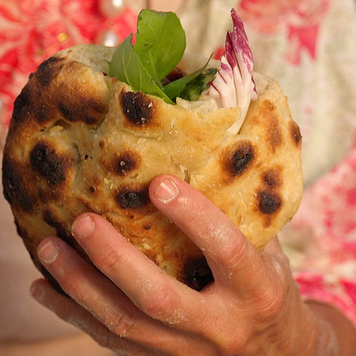 Una mano regge un panino realizzato con l'impasto per pizza e farcito con peperoni, mozzarella, radicchio e basilico.