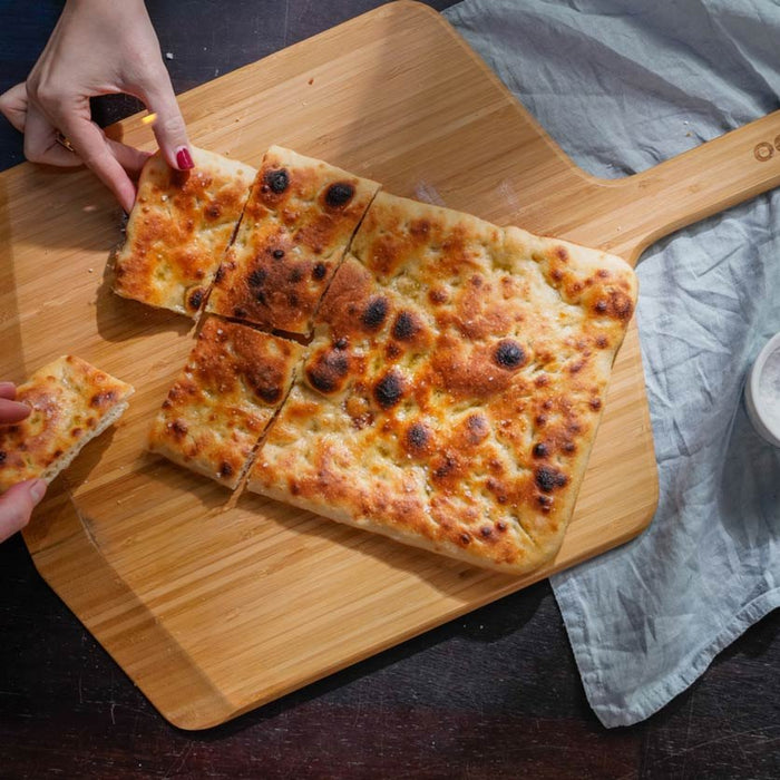 Una pizza bianca romana viene servita su una pala per pizza & tagliere in bambù Ooni.