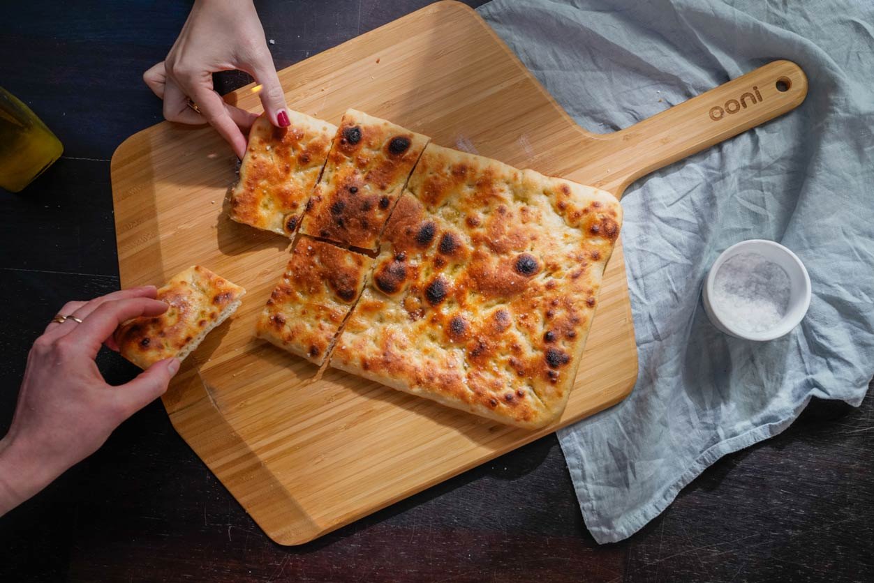 Una pizza bianca romana viene servita su una pala per pizza & tagliere in bambù Ooni.